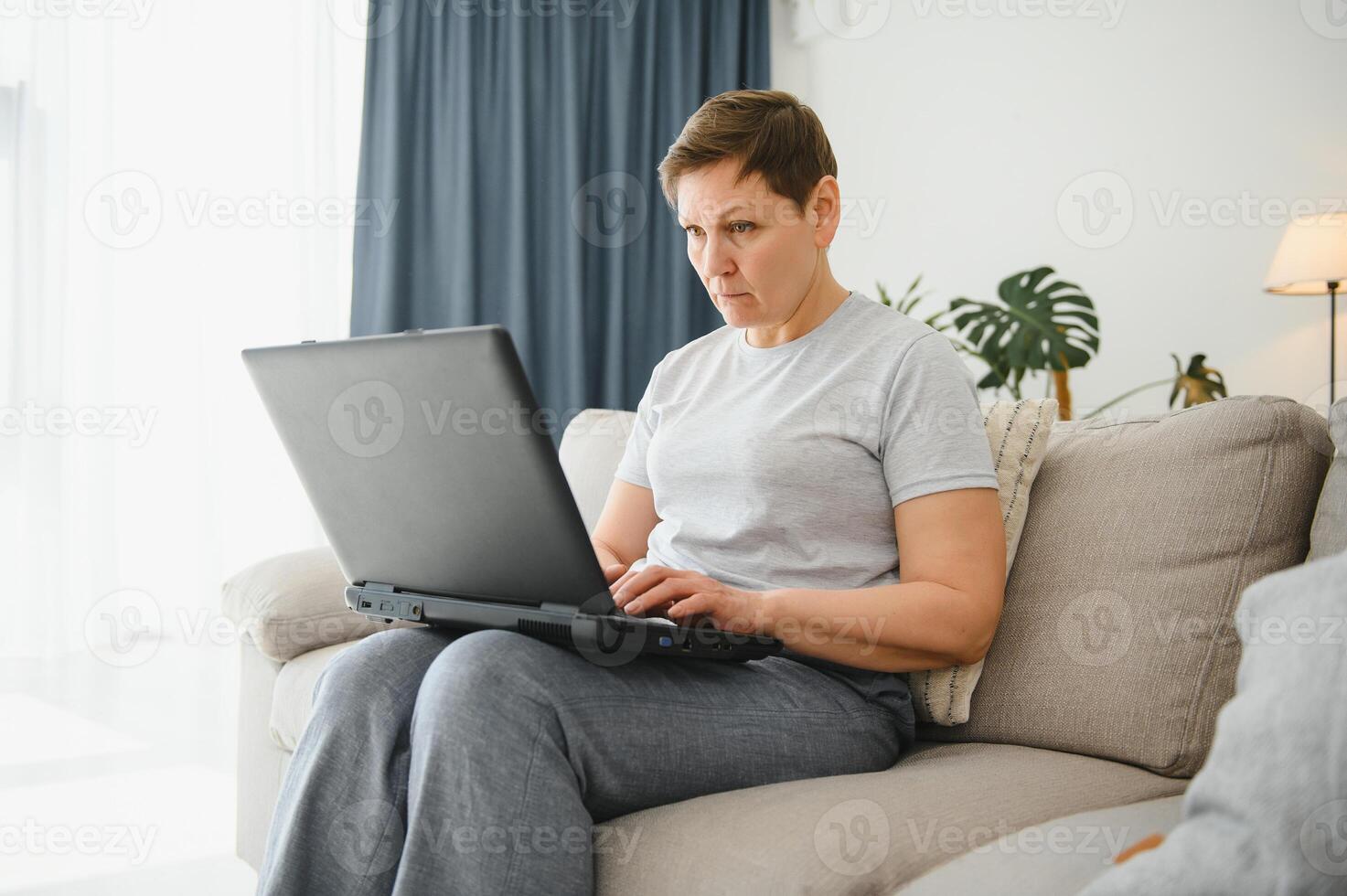 Elderly female sit on couch holding on lap laptop search information, check or typing e-mail, spend time on-line, modern tech, easy interesting pastimes services for retired older generation concept. photo