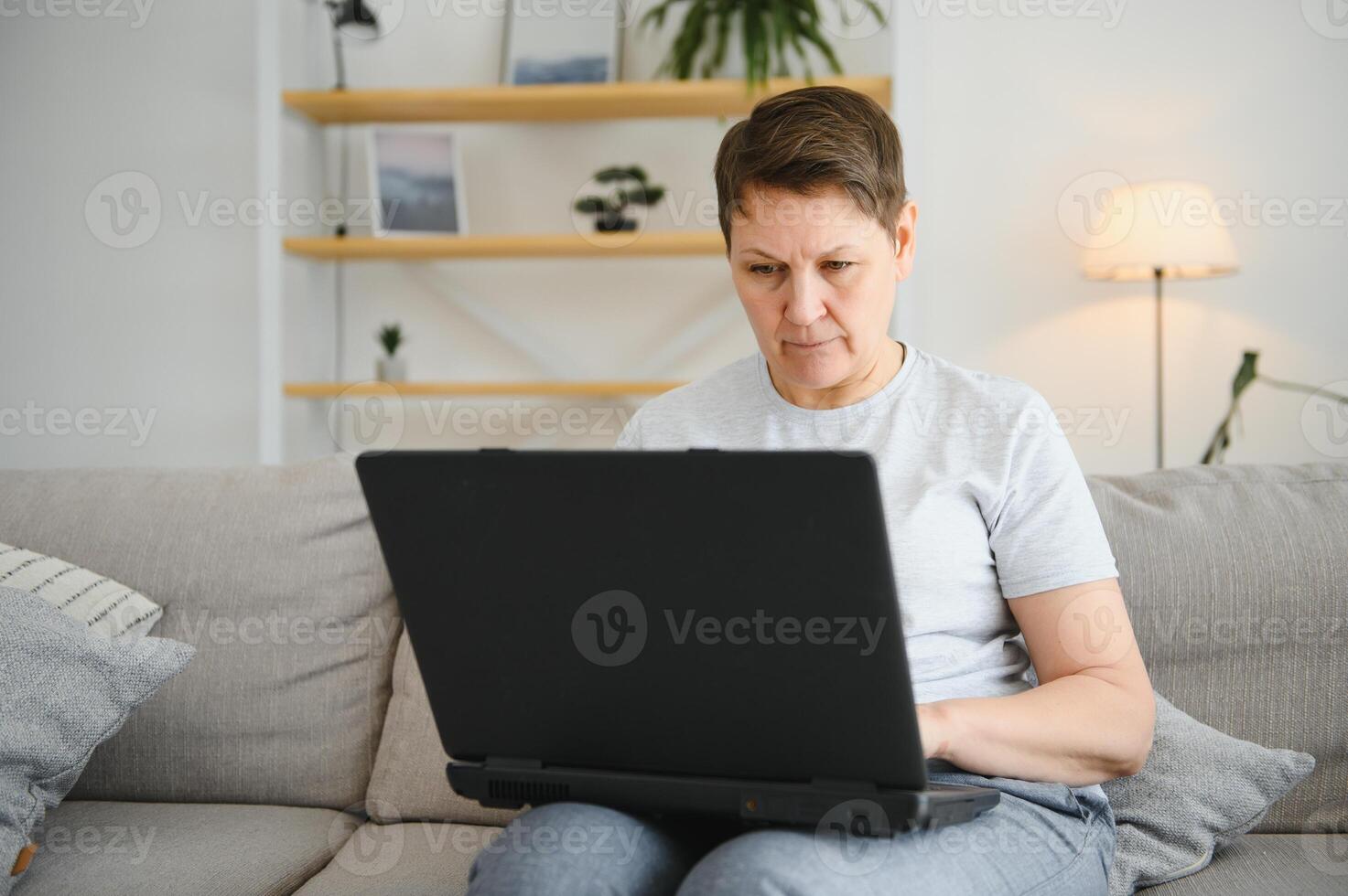 Elderly female sit on couch holding on lap laptop search information, check or typing e-mail, spend time on-line, modern tech, easy interesting pastimes services for retired older generation concept. photo