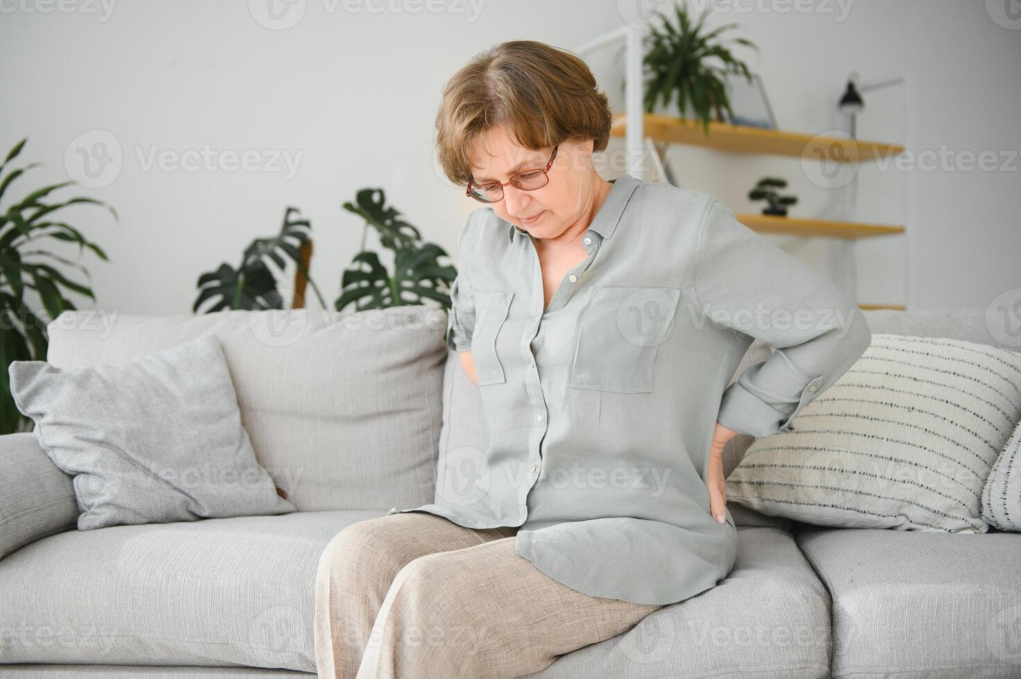 Senior woman suffering from back pain on sofa at home photo