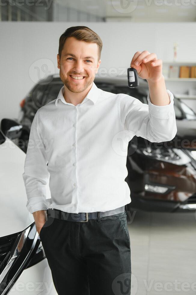 Happy buyer holding keys near the car in front of the modern avtosalon building photo