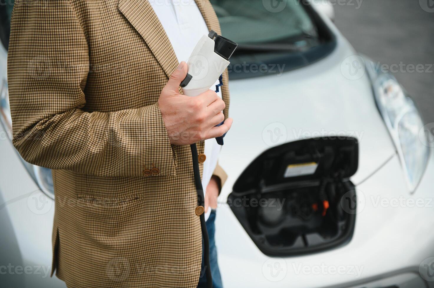handsome man holding charging cable at electric charging station point standing near his new car. photo