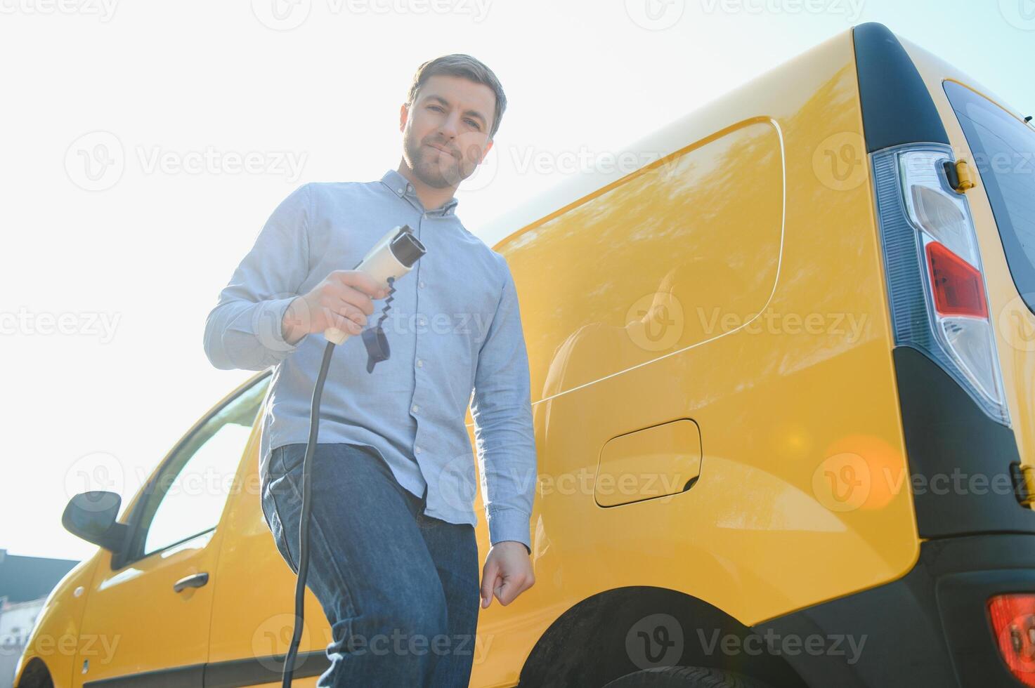young handsome man holding charging cable at electric charging station point standing near his new car photo