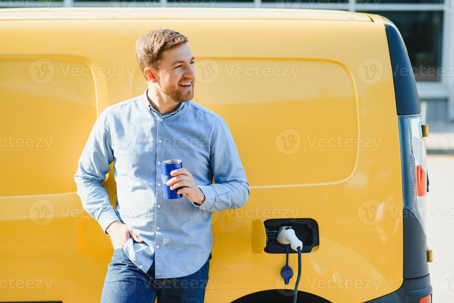 Handsome man drinking coffee while charging electric car photo