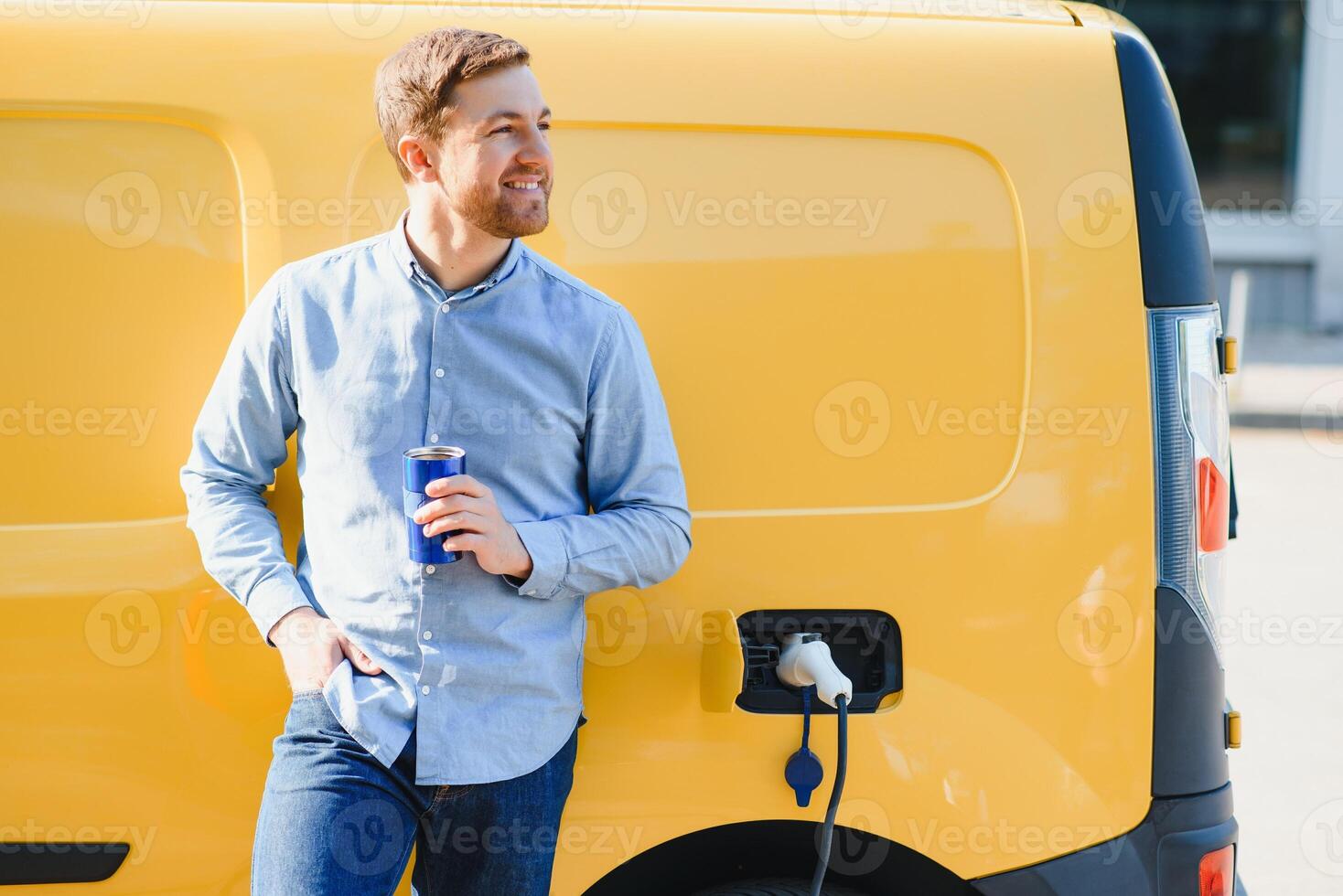 Handsome man drinking coffee while charging electric car photo
