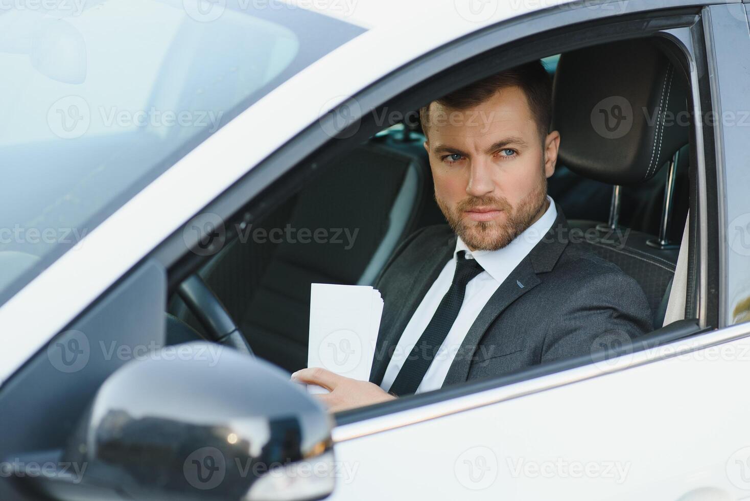 Always in a hurry. Handsome young man in full suit smiling while driving a car. photo