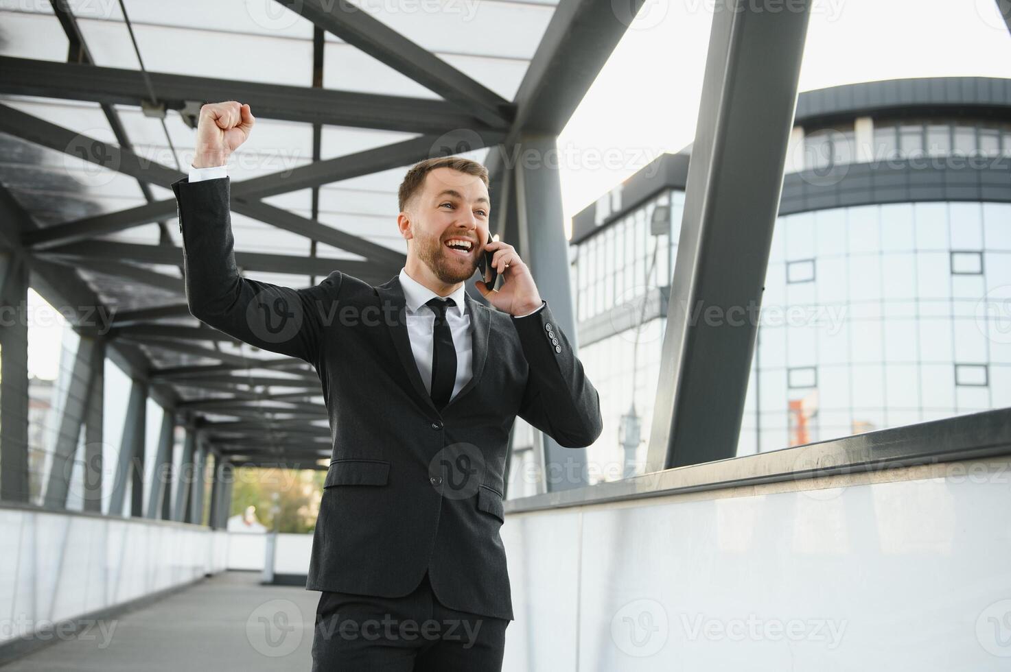 Businessman smiling and raising his fist in the air, with office building background - business success, achievement, and win concepts photo