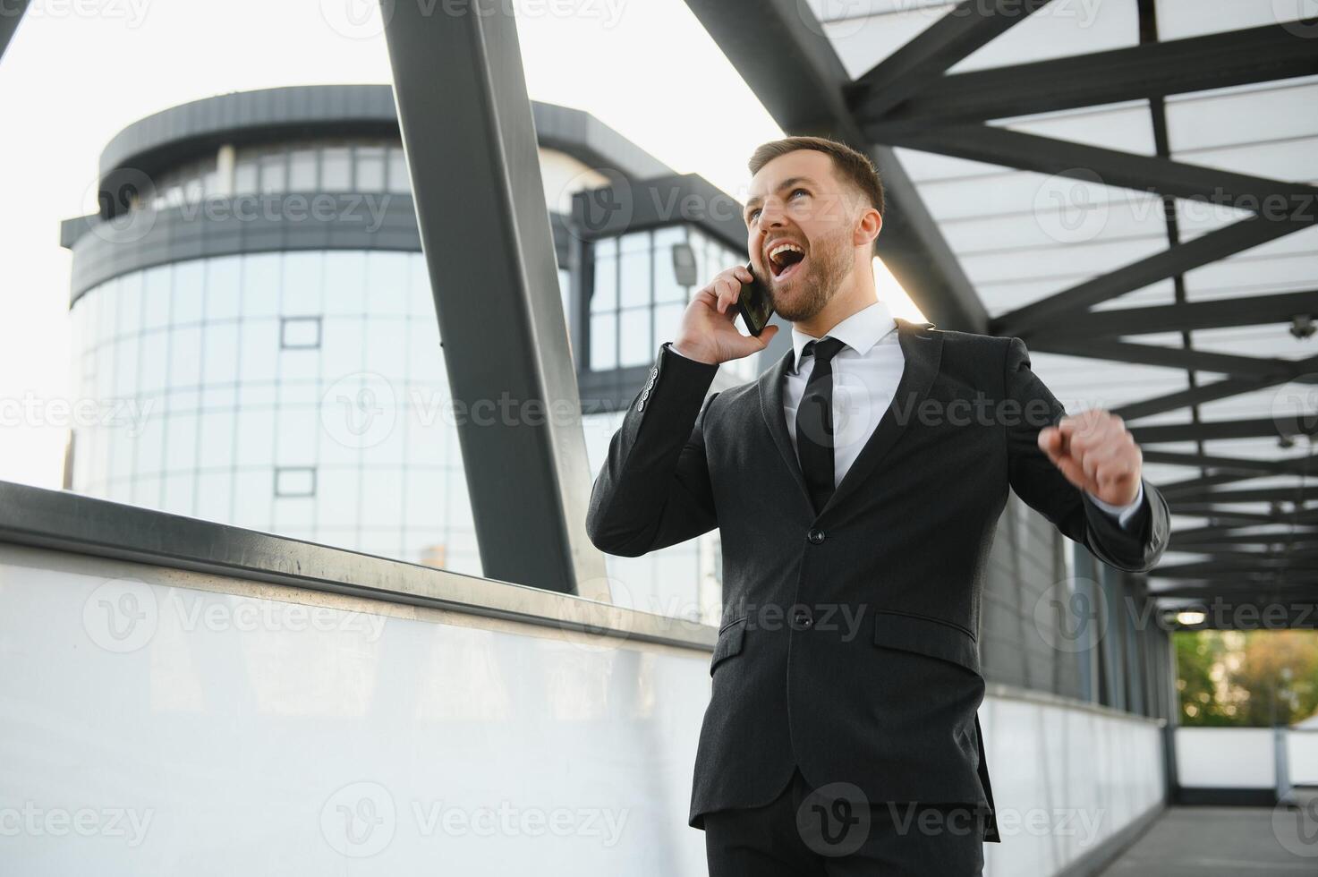 Businessman smiling and raising his fist in the air, with office building background - business success, achievement, and win concepts photo