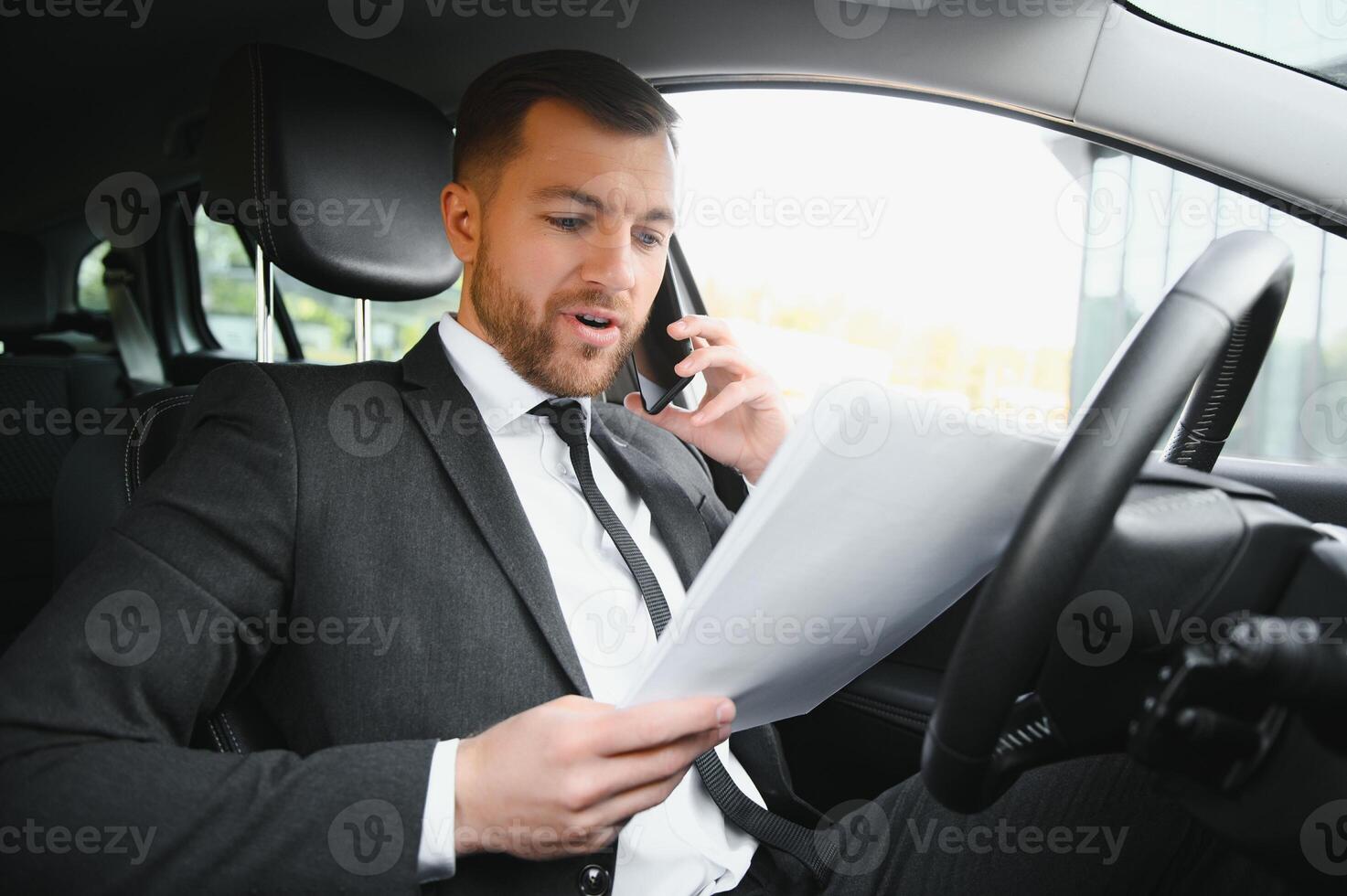 Man of style and status. Handsome young man in full suit smiling while driving a car photo