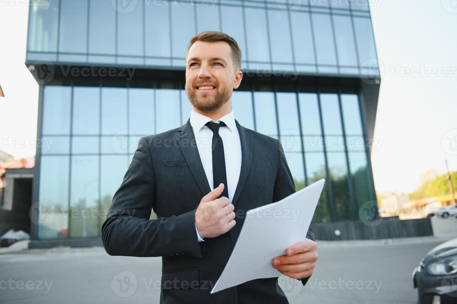 Cheerful young middle-eastern man entrepreneur getting ready before presentation, sitting on the street by office building with backpack, holding papers and drinking coffee, copy space photo