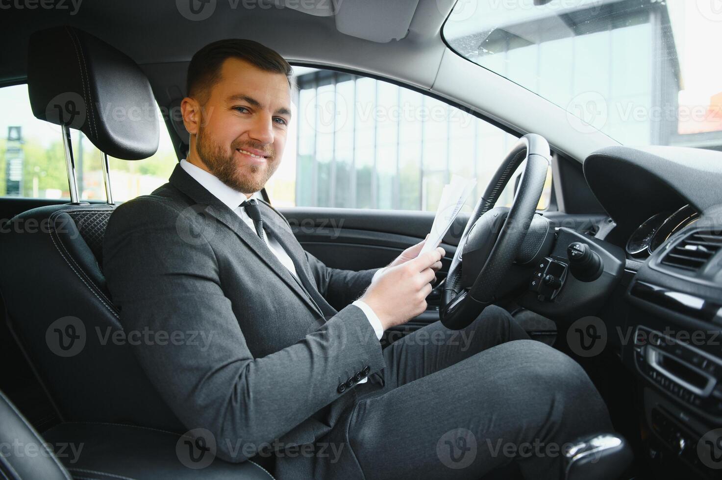 Always in a hurry. Handsome young man in full suit smiling while driving a car. photo