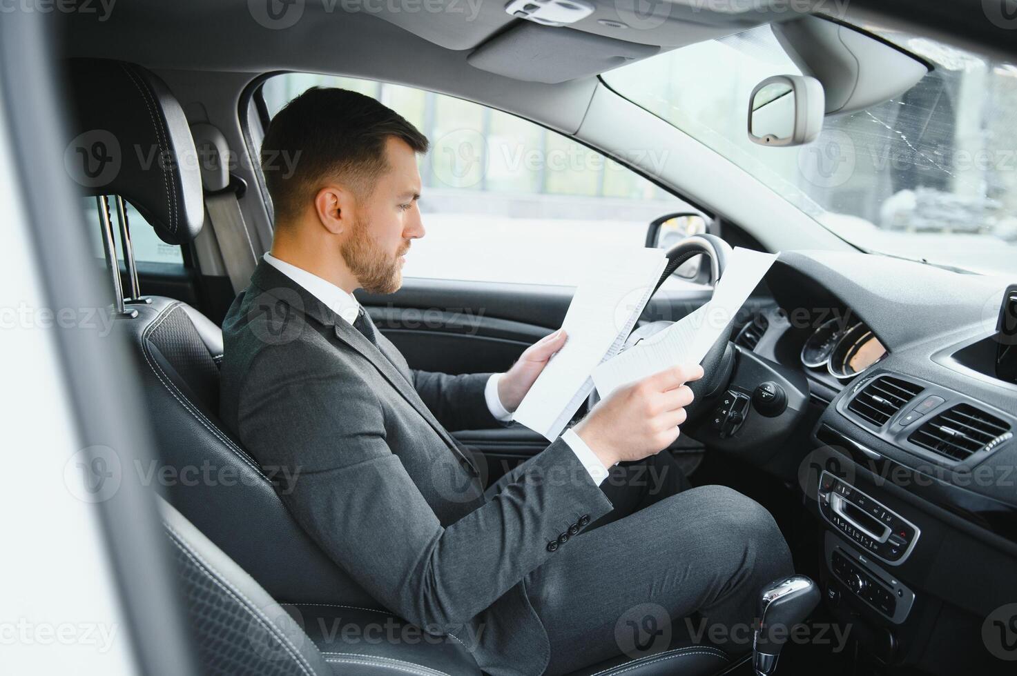 Always in a hurry. Handsome young man in full suit smiling while driving a car. photo