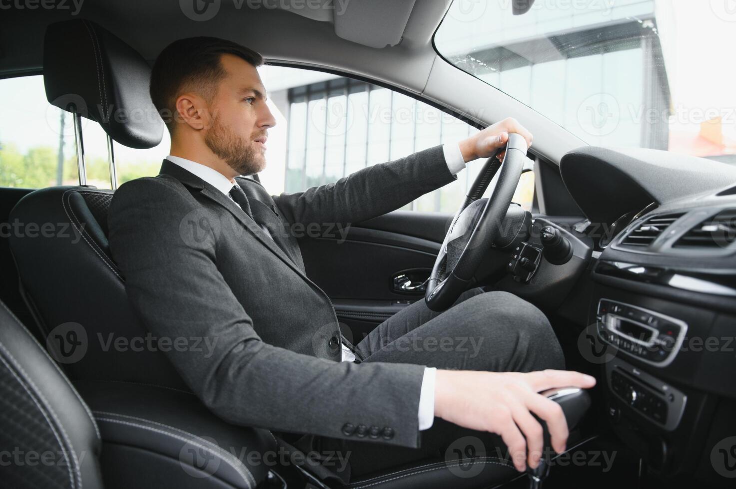 Always in a hurry. Handsome young man in full suit smiling while driving a car. photo