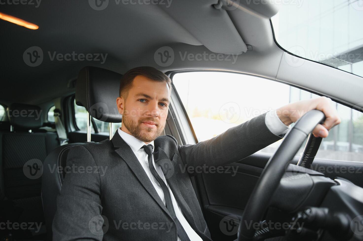 Always in a hurry. Handsome young man in full suit smiling while driving a car. photo