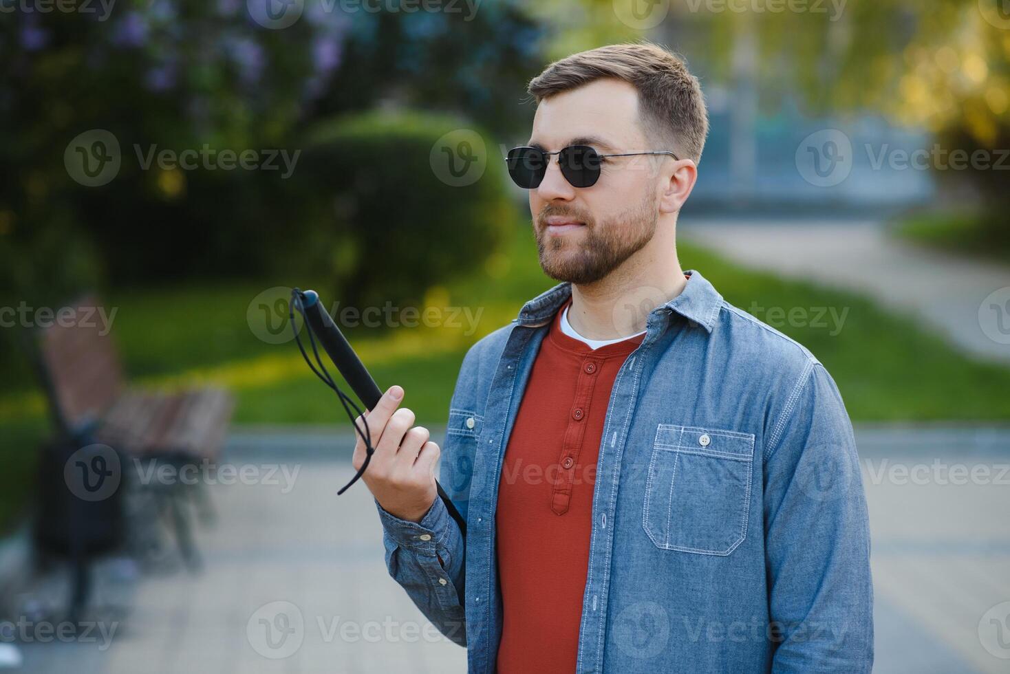 Visually impaired man with walking stick, sitting on bench in city park. Copy space photo