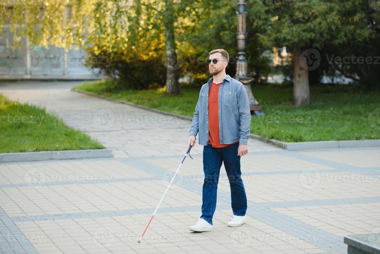 young blind man with white cane walking across the street in city photo