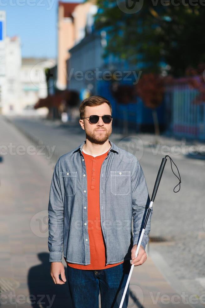 Young handsome blinded man walking with stick in town photo