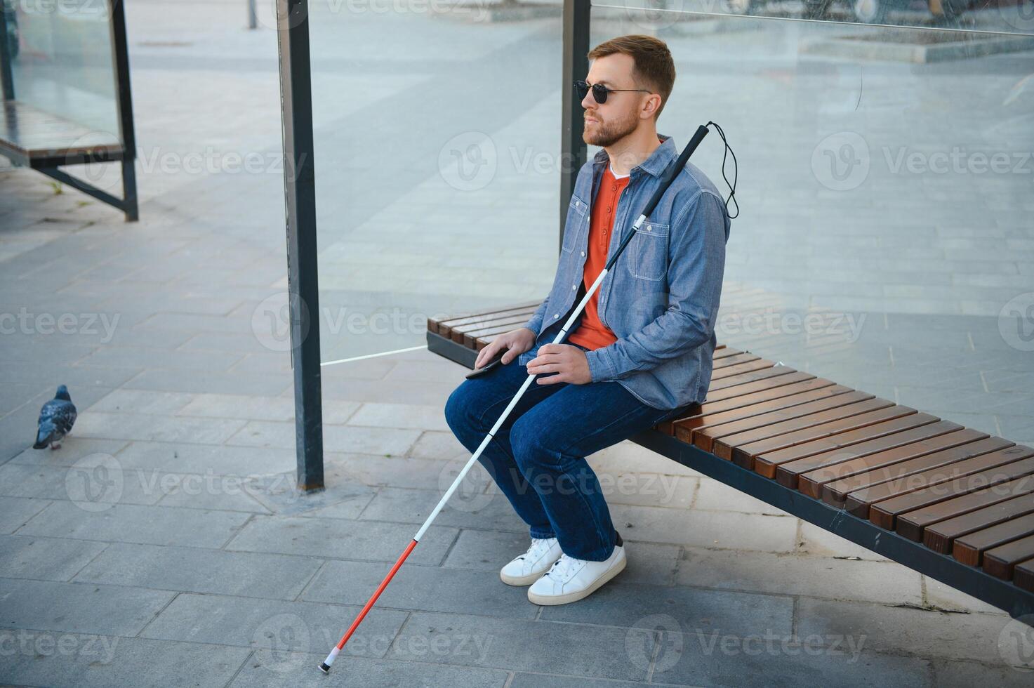 Visually impaired man with walking stick, sitting on bench in city park. Copy space photo