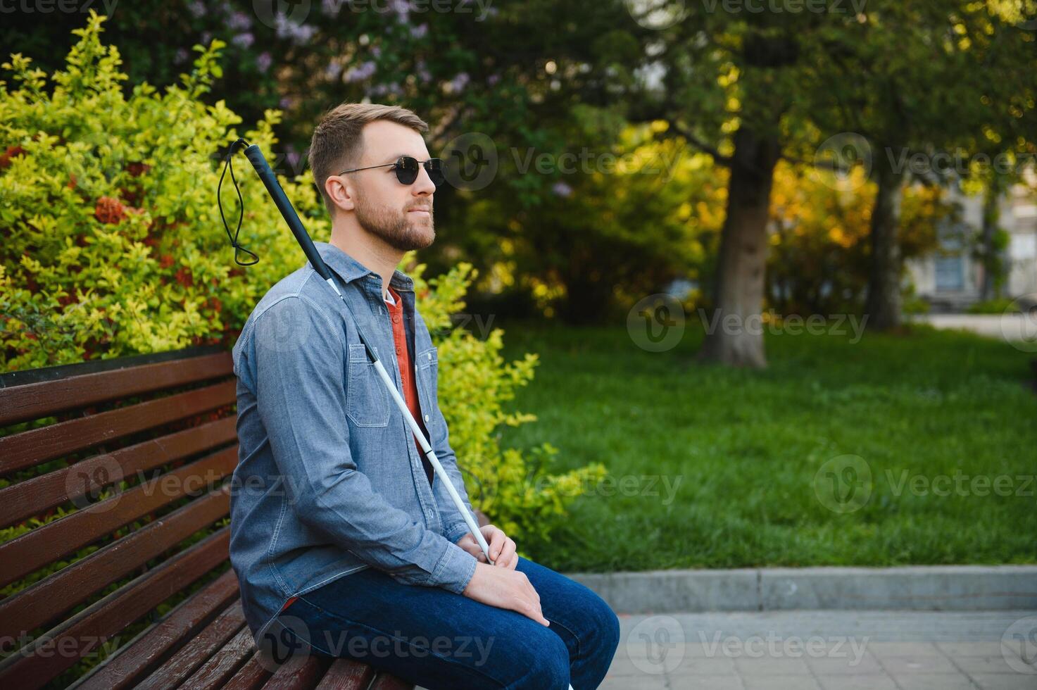 Young handsome blinded man walking with stick in town photo