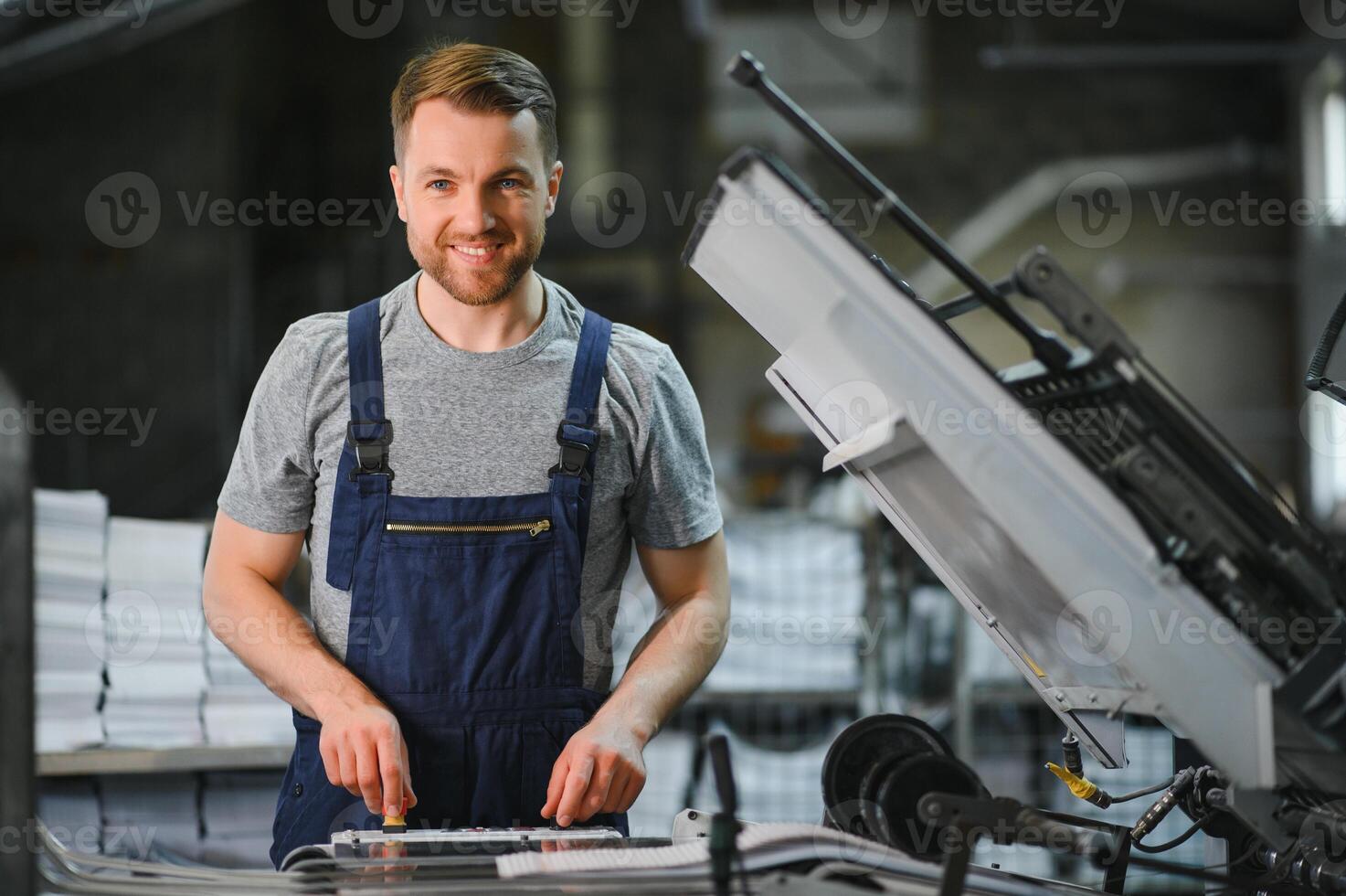 Portrait of production line worker controlling manufacturing process of modern packaging industrial machine in printing factory photo