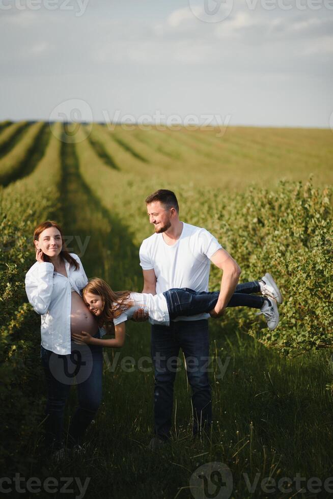 Happy pregnant couple with daughter in summer nature. photo