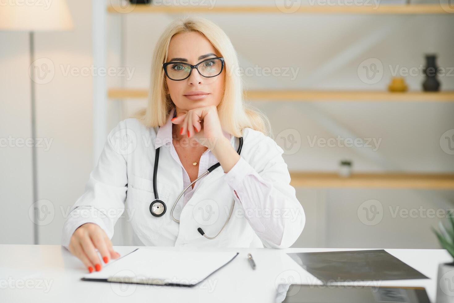 Portrait shot of middle aged female doctor sitting at desk and working in doctor office photo