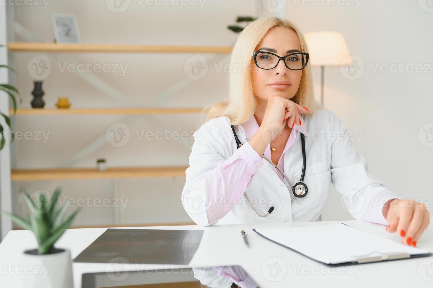 Portrait shot of middle aged female doctor sitting at desk and working in doctor office photo