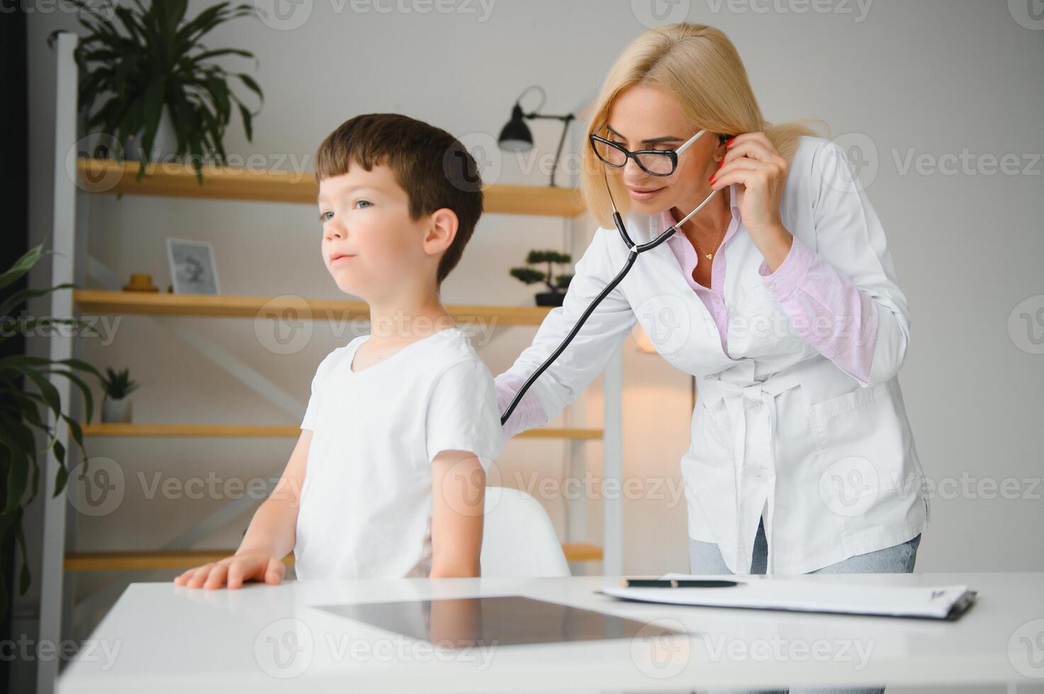 Pediatrician listening to breathing in the lungs and heartbeat with stethoscope. Portrait of adorable little boy visiting doctor. photo