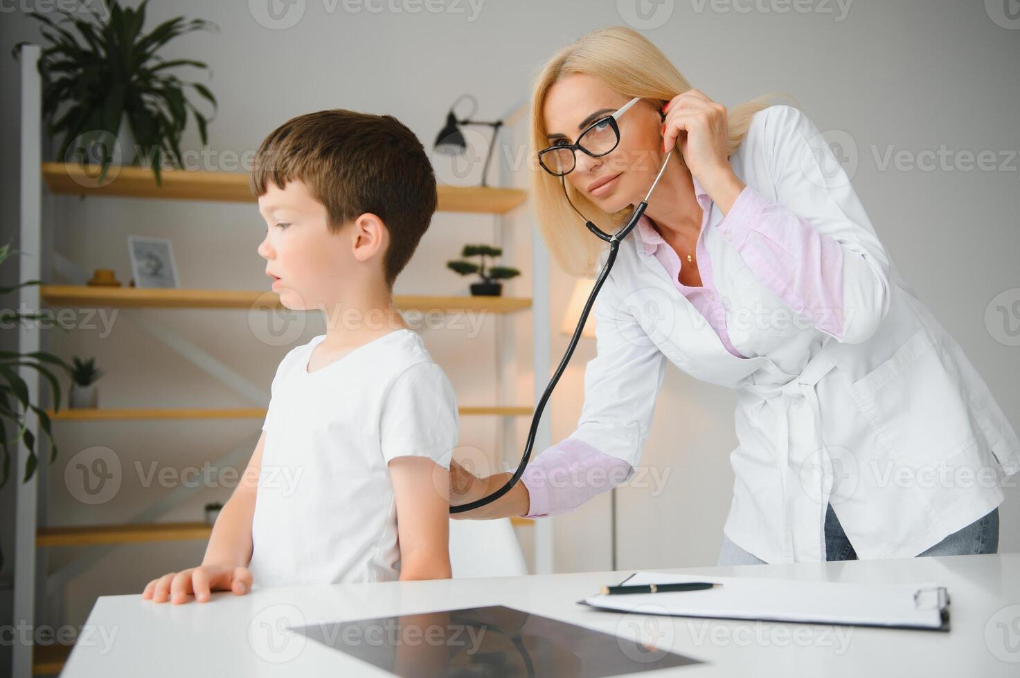 Pediatrician listening to breathing in the lungs and heartbeat with stethoscope. Portrait of adorable little boy visiting doctor. photo