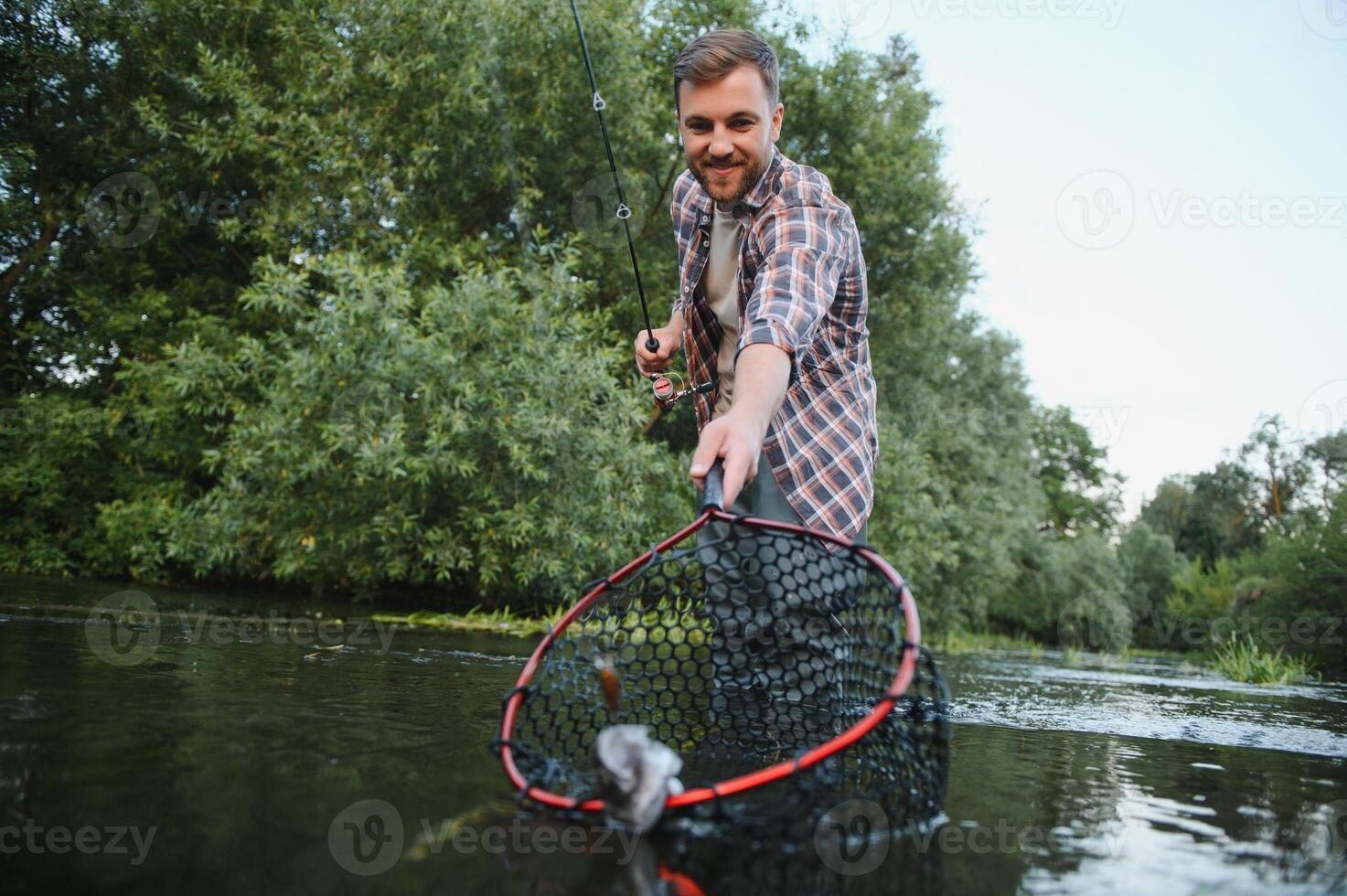 Man with fishing rod, fisherman men in river water outdoor. Catching trout fish in net. Summer fishing hobby photo