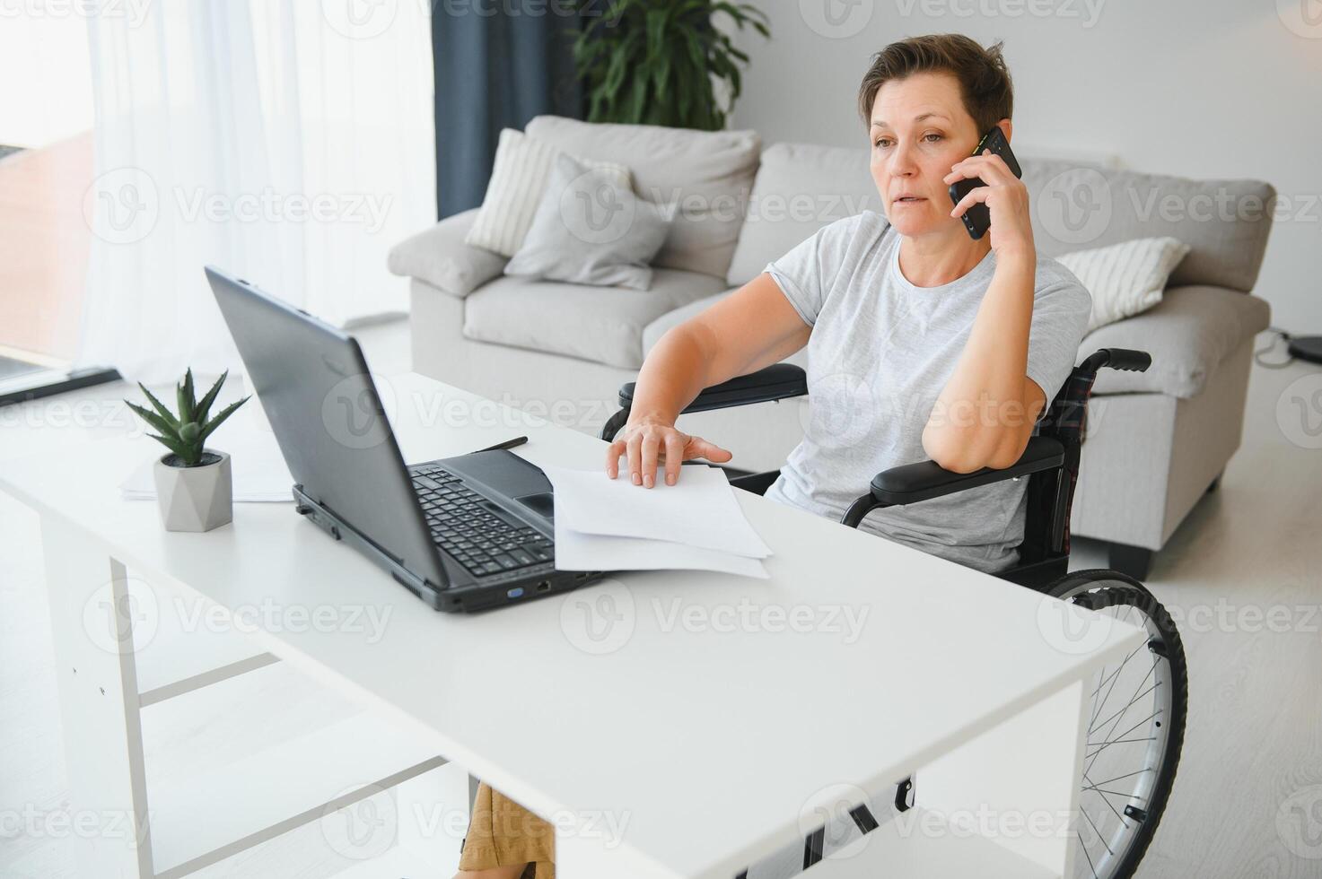 Freelancer in wheelchair using laptop near notebook and papers on table photo