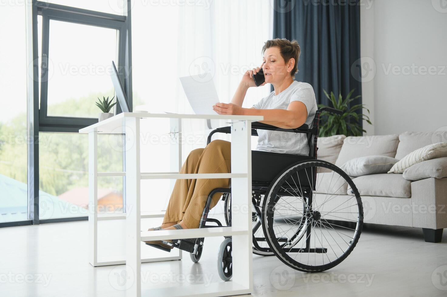Positive elderly woman in wheelchair working on laptop, IT freelancer, online photo
