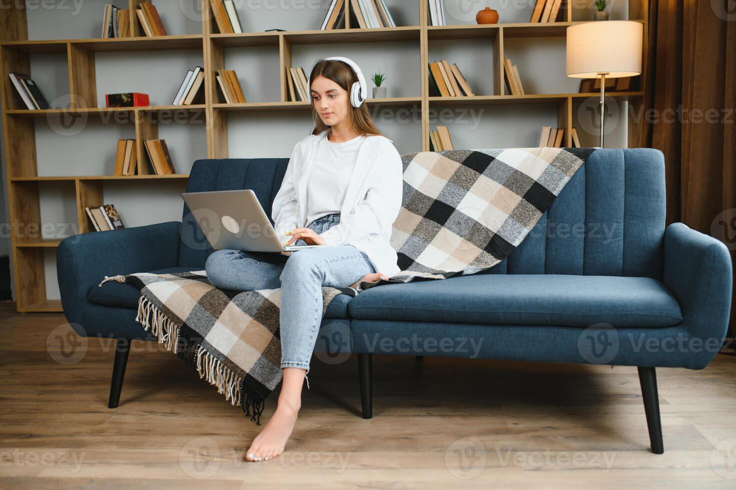Smiling attractive young woman sitting on sofa using laptop communicating working online at home, happy teen girl typing on computer, enjoying writing blog or chatting with friends in social network photo