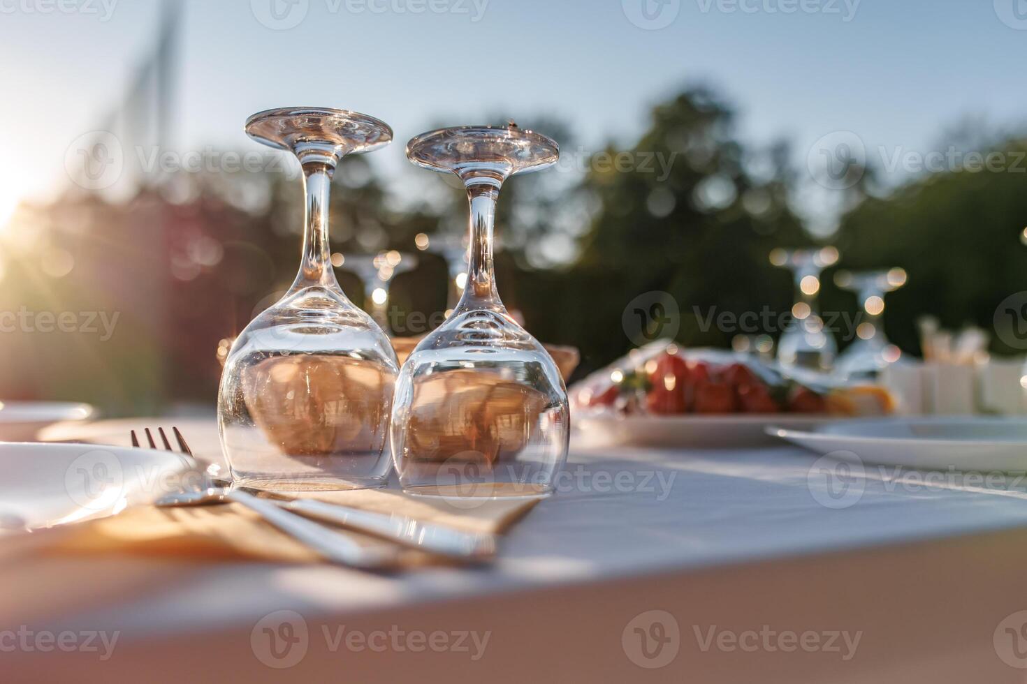 empty wine glasses on banquet served table in open air in rays of setting sun photo