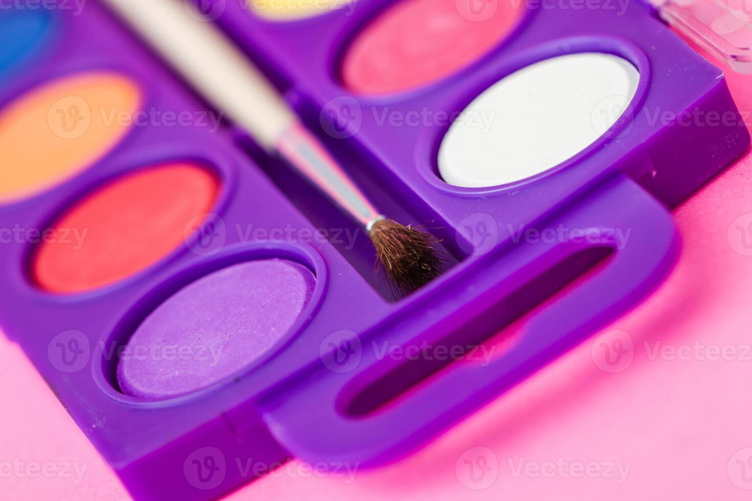 Close up of a watercolor paint palette with a paintbrush, vibrant colors on a pink background. photo