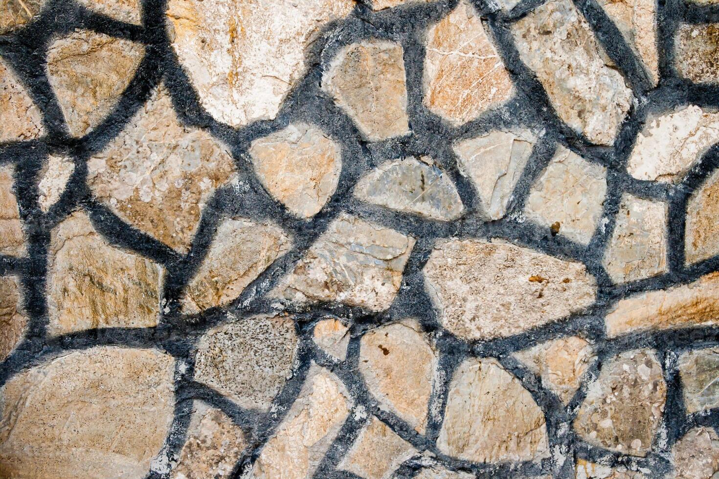 Close up of a stone wall with irregularly shaped stones and dark mortar lines, texture, background. photo