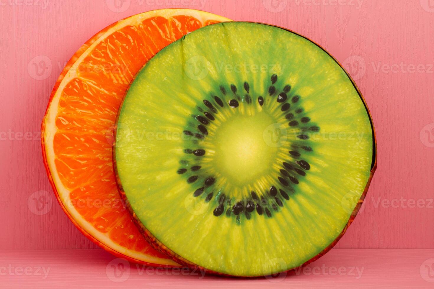 Halved orange and a halved kiwi pillows placed side by side against a pink background. photo