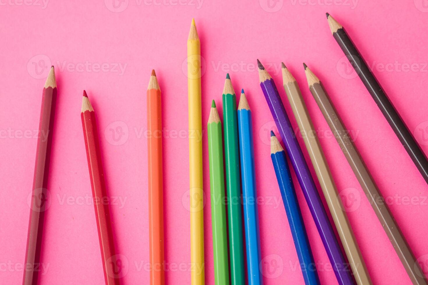 Colorful pencils scattered playfully on a vibrant pink background. photo