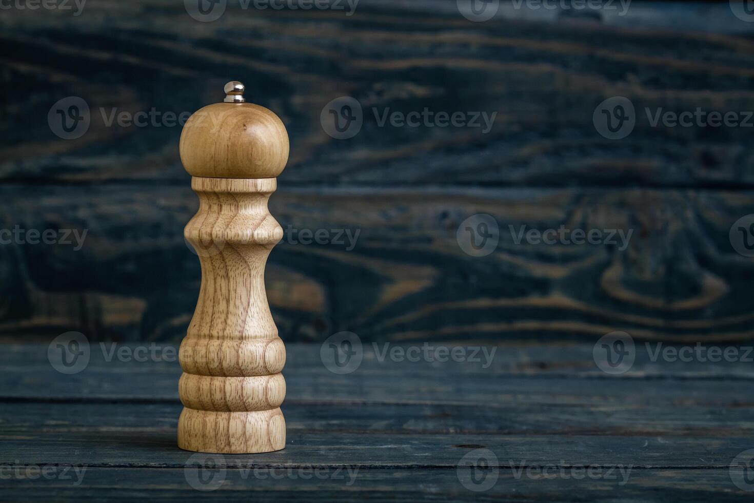 Wooden pepper mill placed on a dark blue wooden surface, with copy space. photo