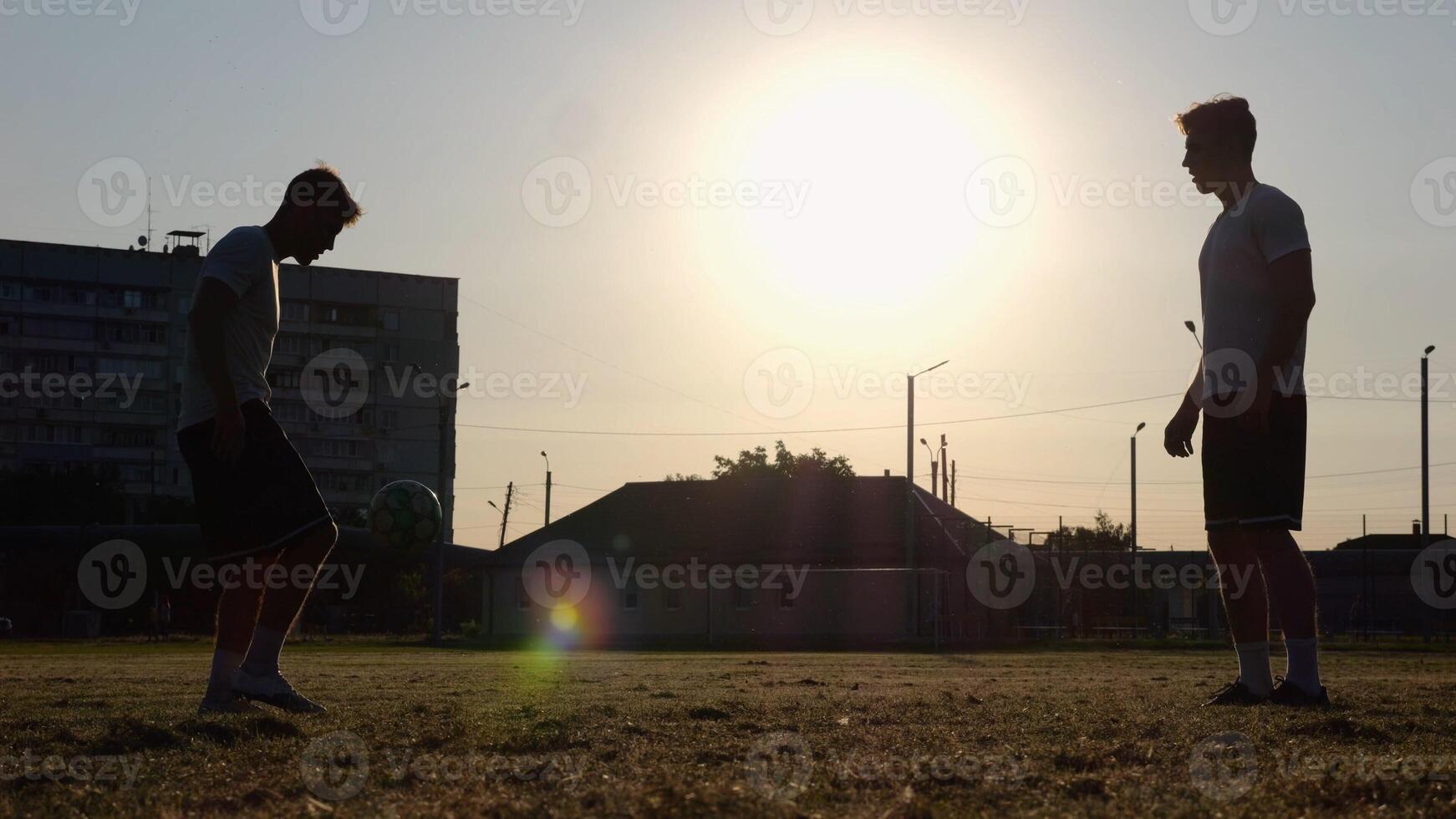Silhouette of professional footballers kicking soccer ball with their heads on stadium at sunset. Two sportsmen showing tricks with ball while passing it to each other at field. Freestyle football photo