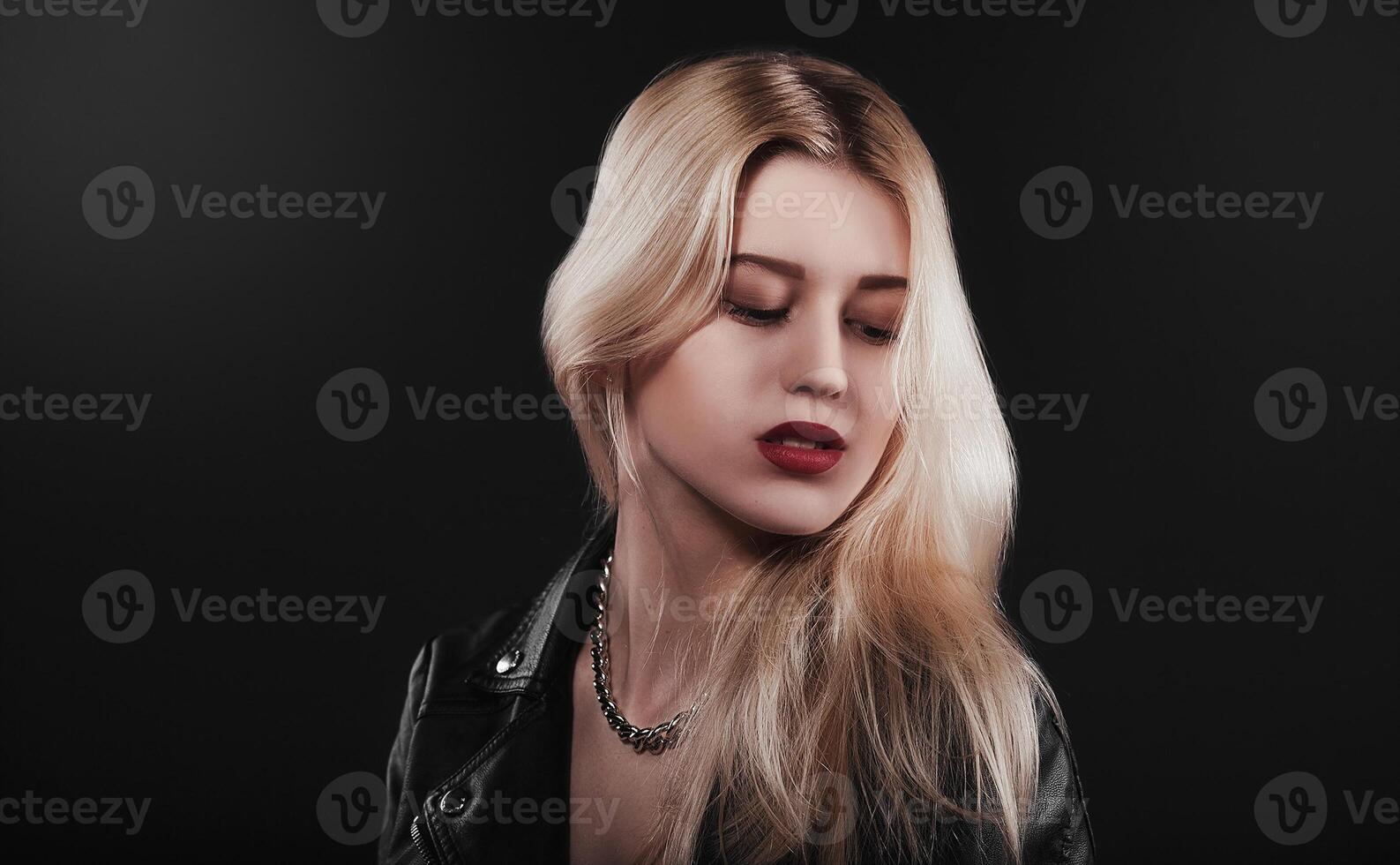 A beautiful, glamour young blond Girl dressed in a black jacket is posing on black background photo