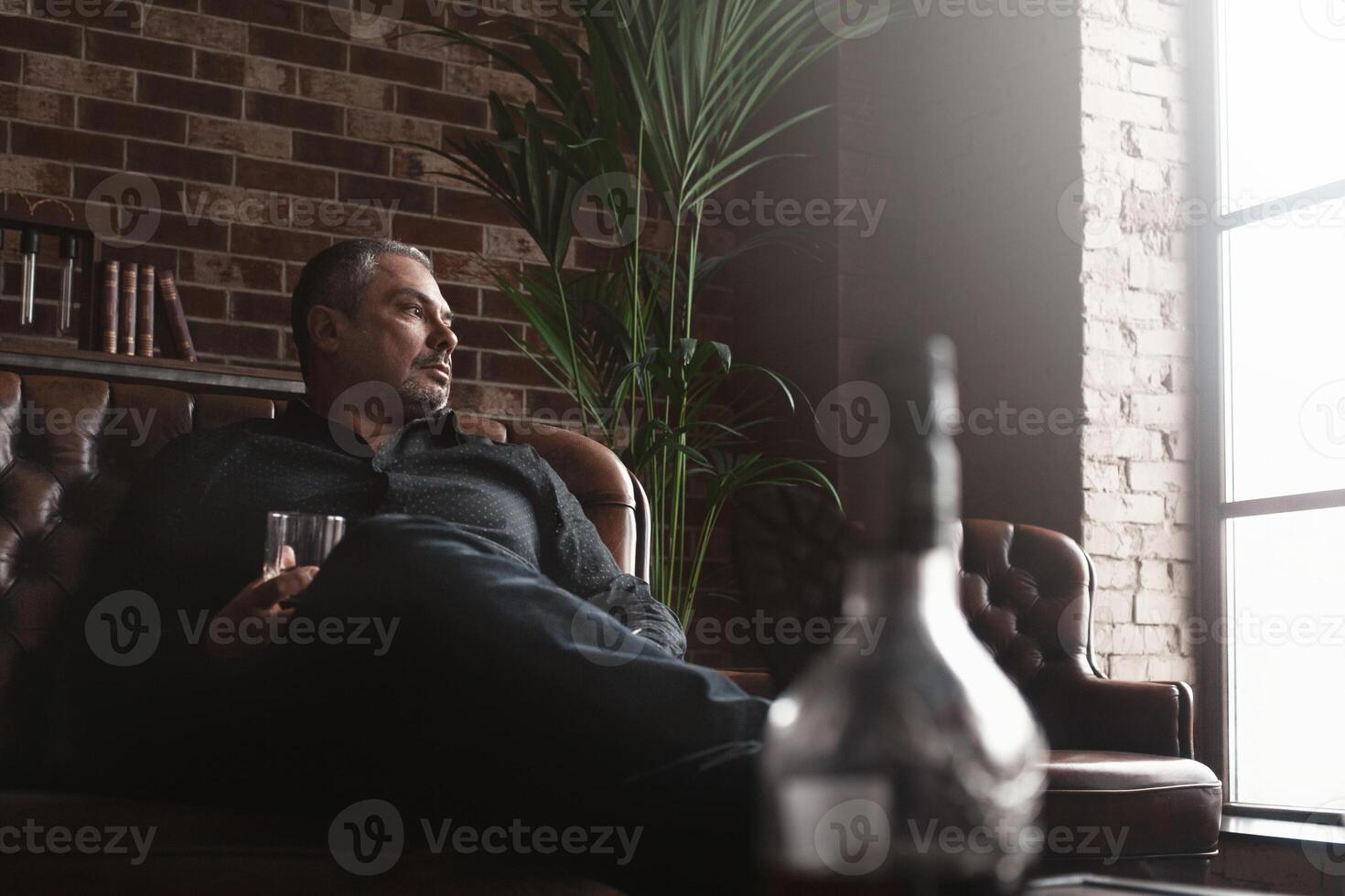 Relaxing after a hard working day. Confident mature businessman sitting at home and drinking whiskey photo