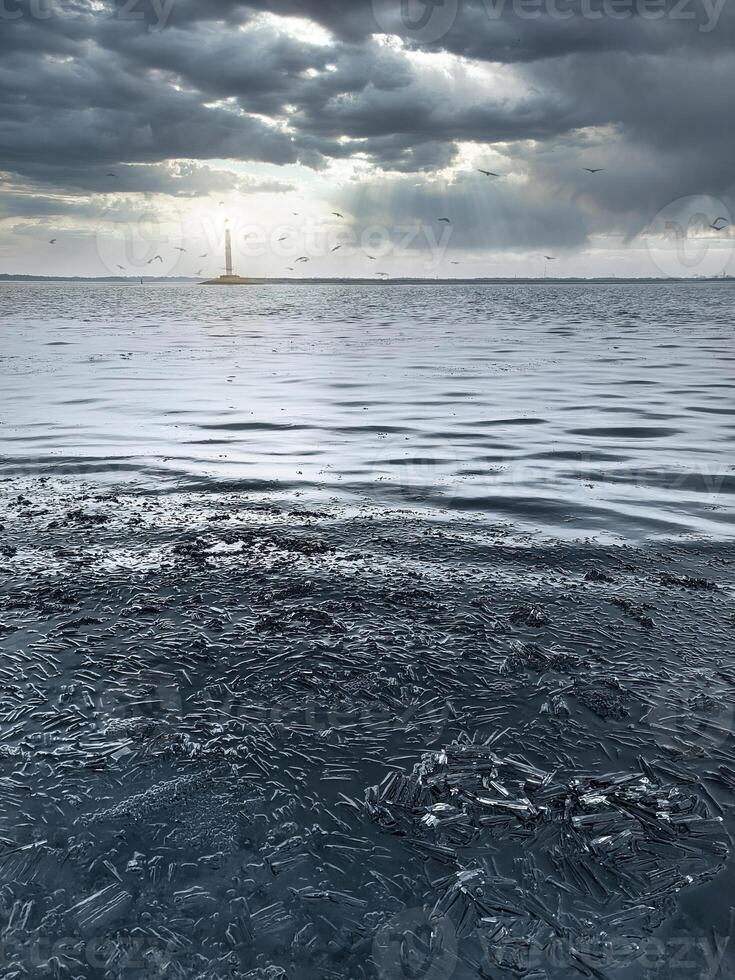 Blue winter ice - a winter scene with blue ice with a lighthouse glowing in the distance, against a background of beautiful overcast clouds. photo