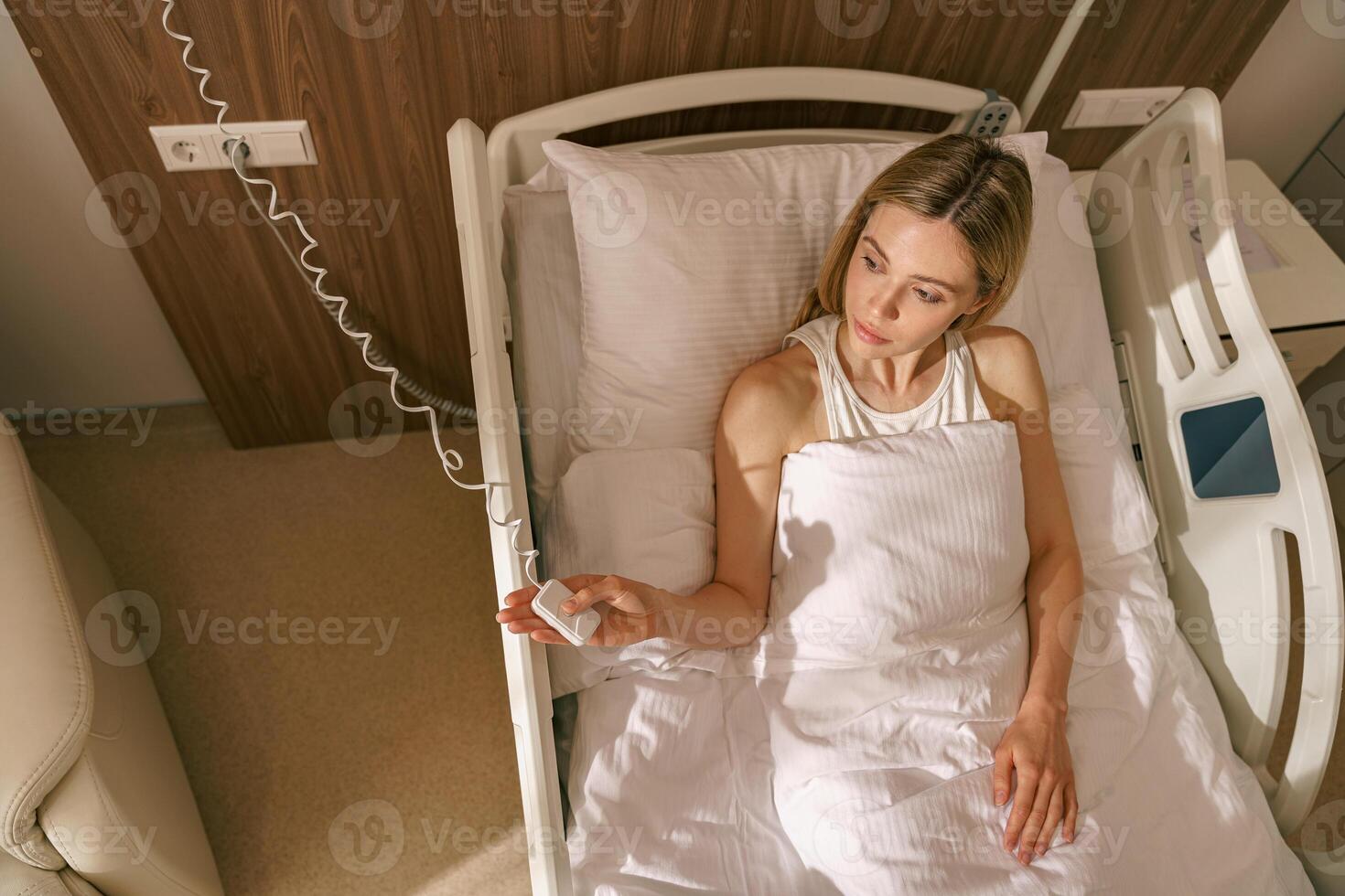 Top view of woman patient holding emergency call button while lying in hospital bed photo