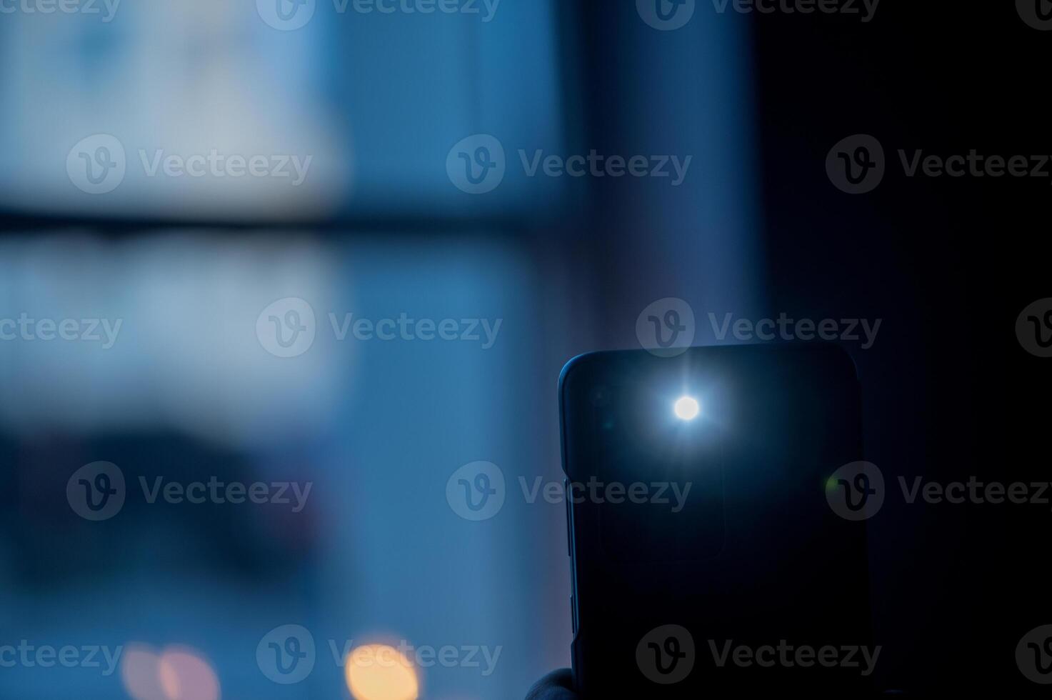 Male hand holds a smartphone with a burning flashlight with lighting window on the background photo