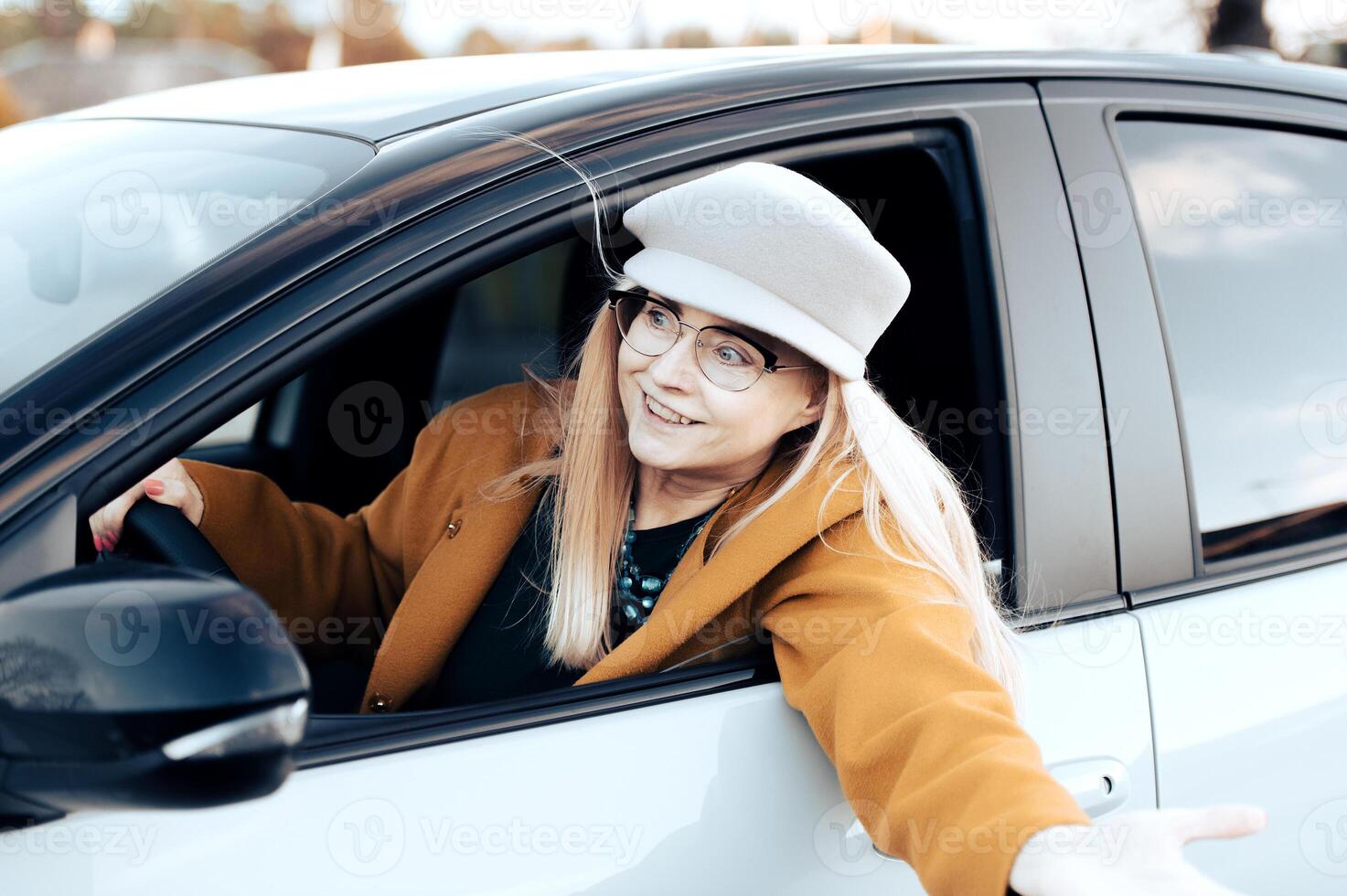 excited middle aged flirtatious woman holding steering wheel gesturing and driving car photo