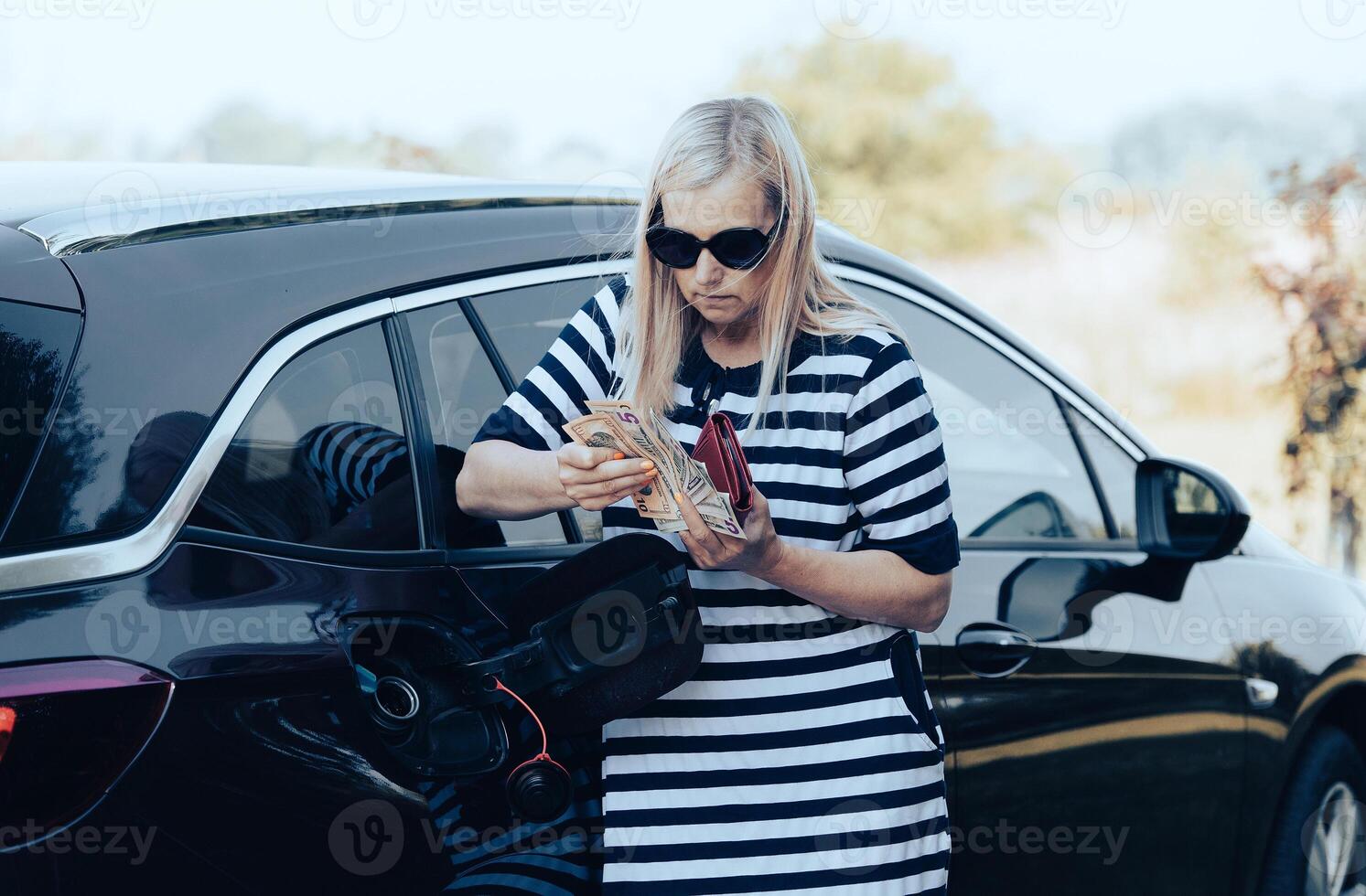 Desperate woman hold cash dollar bills next to car with an open tank, concept of rising fuel prices photo