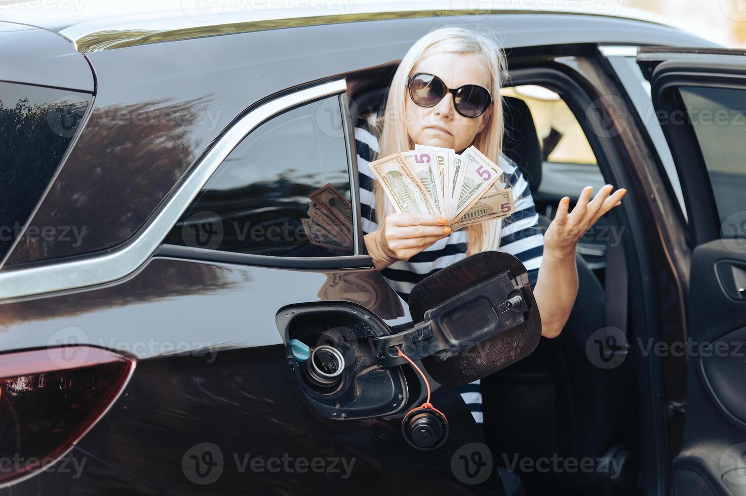 Desperate woman hold cash dollar bills next to car with an open tank, concept of rising fuel prices photo