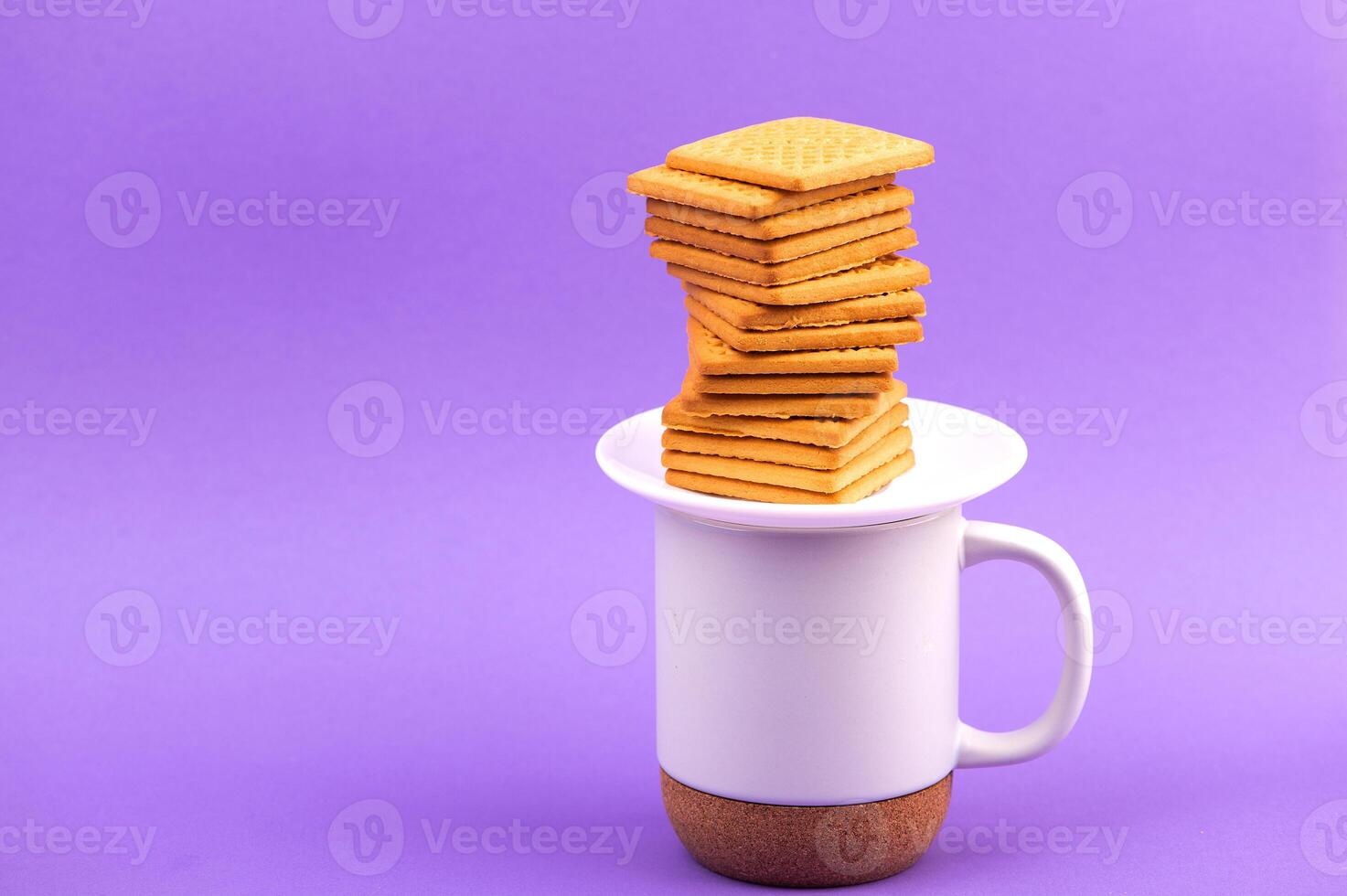 Cookies and cup of coffee. Stacks of tasty cookies on the white plate. Square biscuits on the violet background with copy space. Healthy eating photo