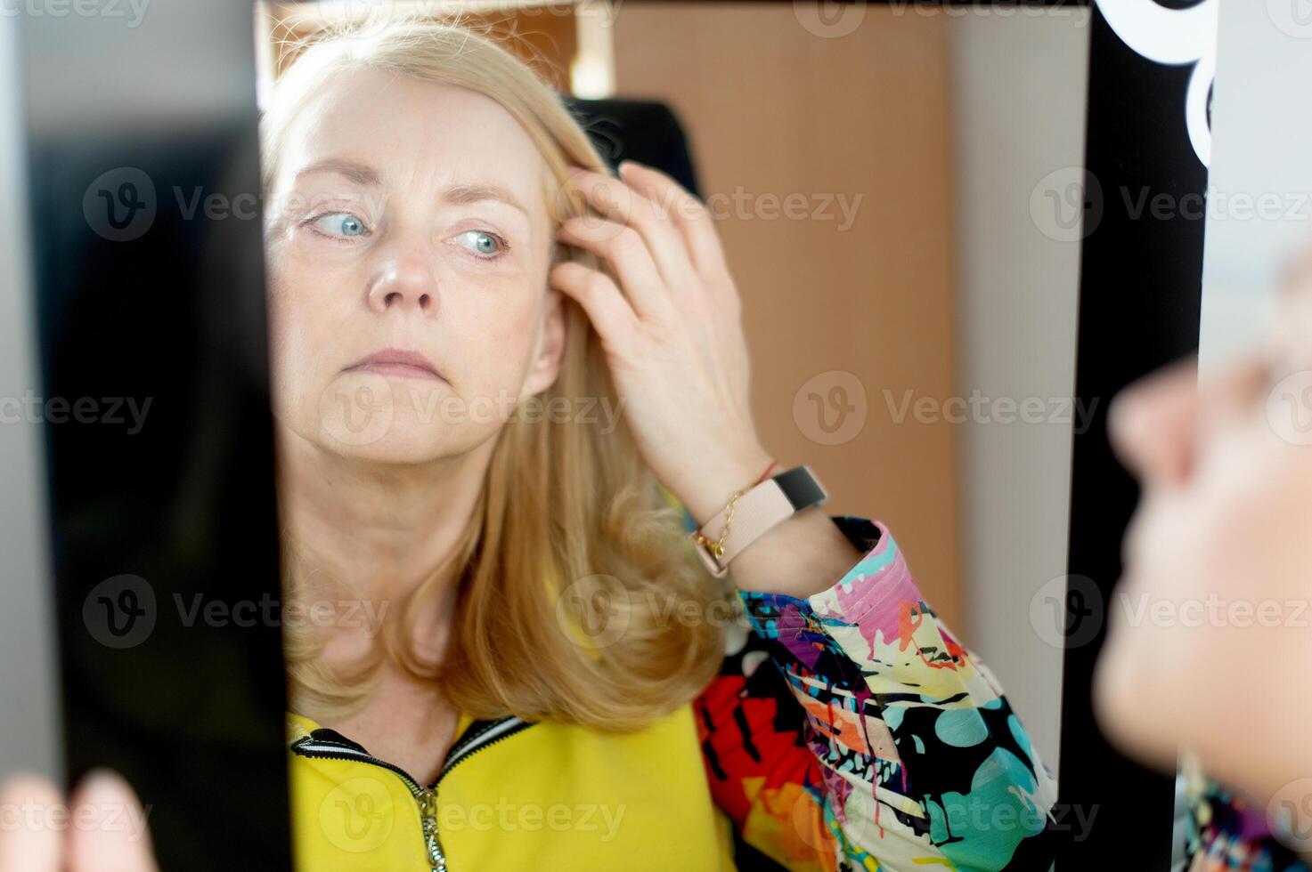 Portrait of middle-aged woman looking at her face in mirror, skin aging concept photo
