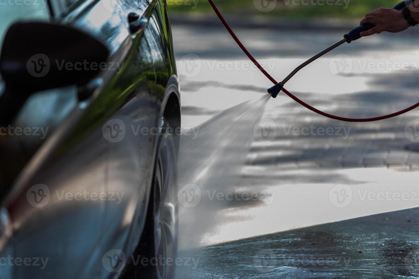 Car washing. Mature caucasian man cleaning automobile using high pressure jet water photo